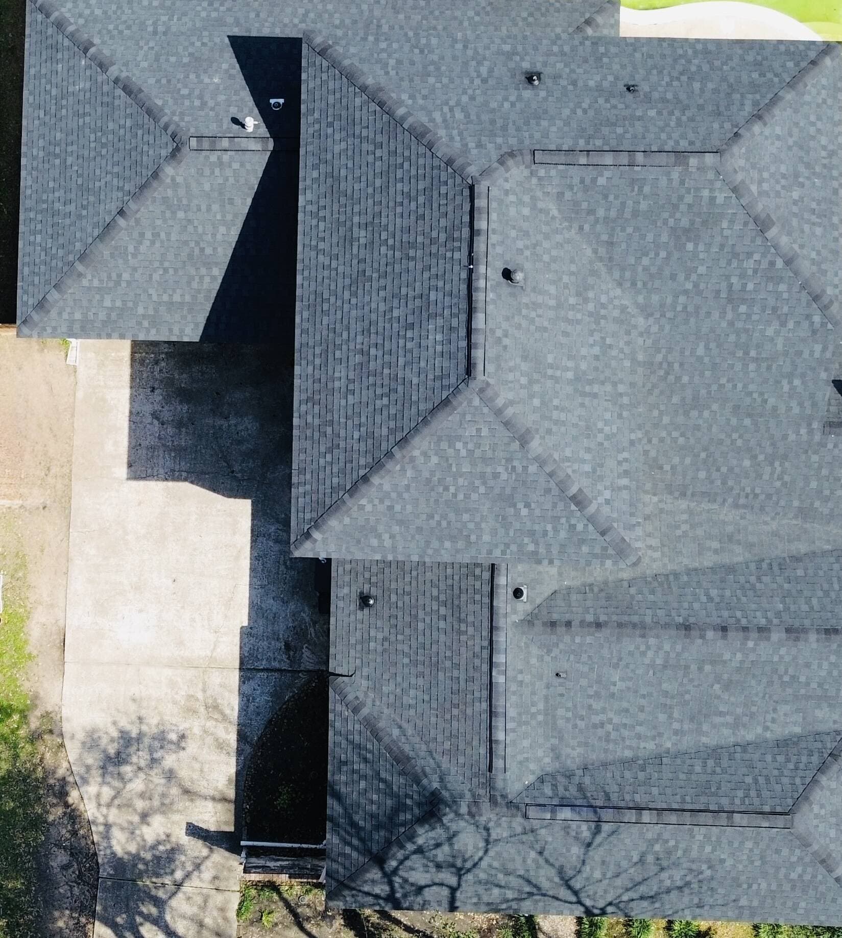 Top-down drone view of a completed dark architectural shingle roof with clean hip and ridge lines