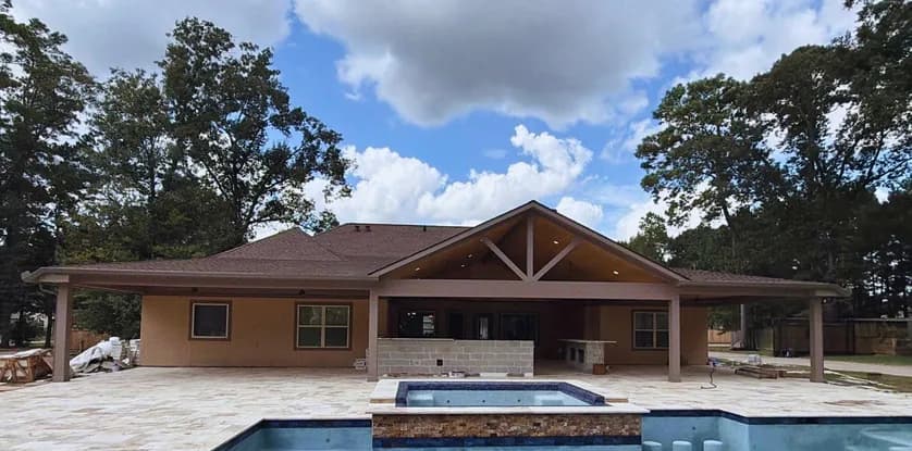 Finished vaulted patio cover with a gabled center section across the back of a single-story stucco home, seen from the far side of the pool